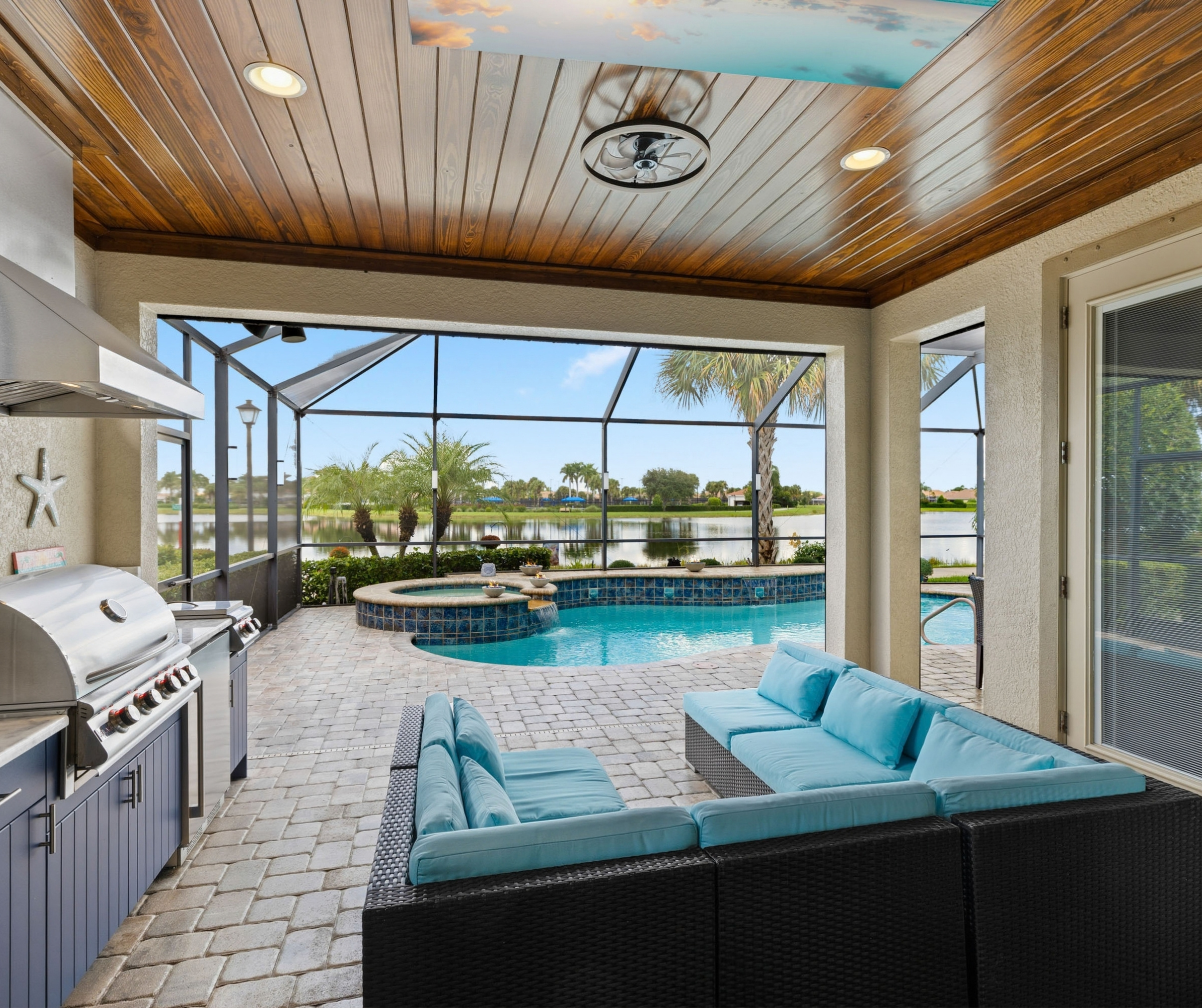 Stained wood plank lanai ceiling over an outdoor kitchen and lounge with a pool and lake view
